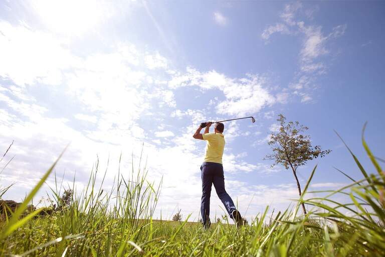 Ein männlicher Golfer, gekleidet in passender Kleidung, schwingt seinen Golfschläger auf einem sonnigen Golfplatz in Bad Füssing.